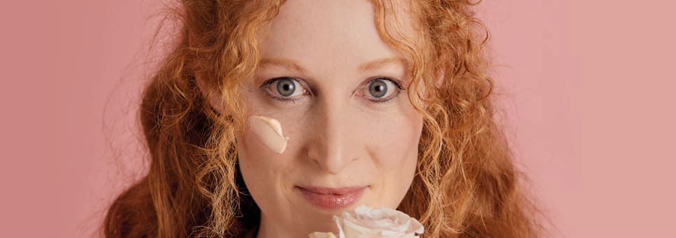 Frau mit Creme auf der Wange schnuppert an einer Rose